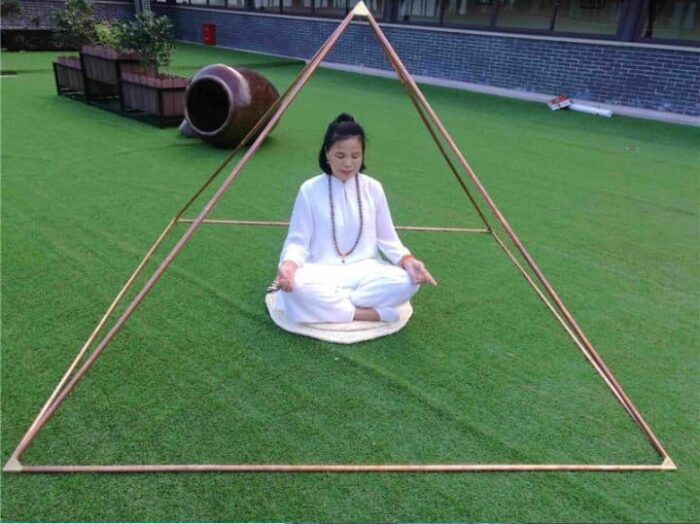 A woman in white sitting cross-legged inside a Meditation Pyramid