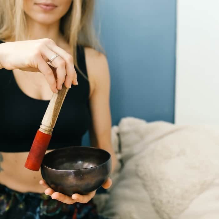 a modern woman circling the wooden mallet on a Tibetan singing bowl