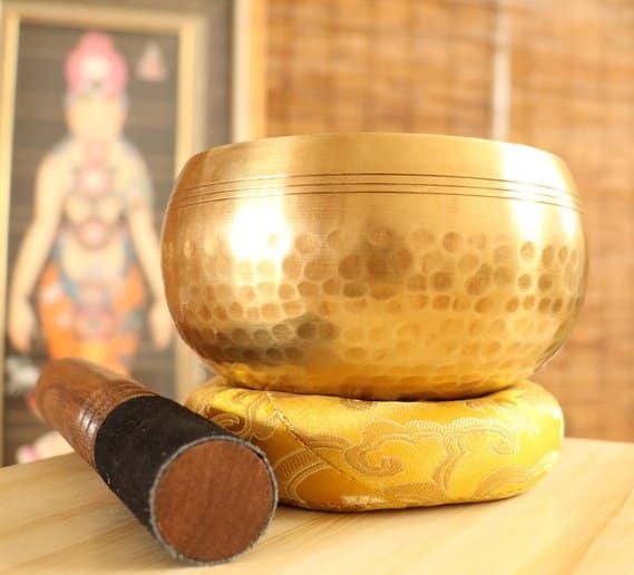 Handmade brass singing bowl on cushion next to a mallet