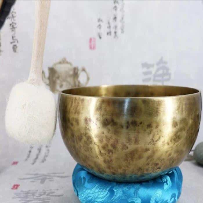 A Tibetan singing bowl on a blue cushion being rung by a white-tipped mallet