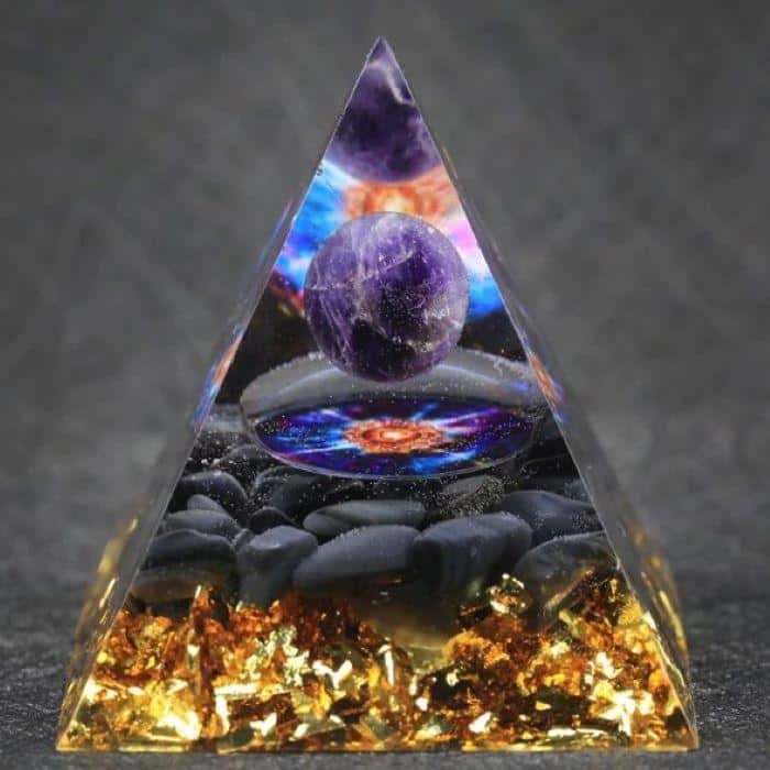 A close-up of an orgonite meditation pyramid with a golden base and space-themed design