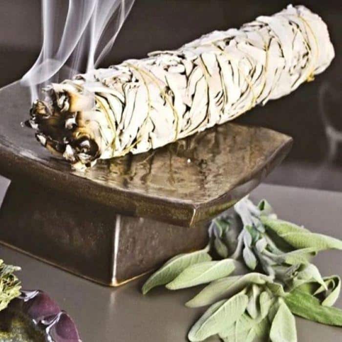 A smoking sage meditation bundle on a ceramic altar